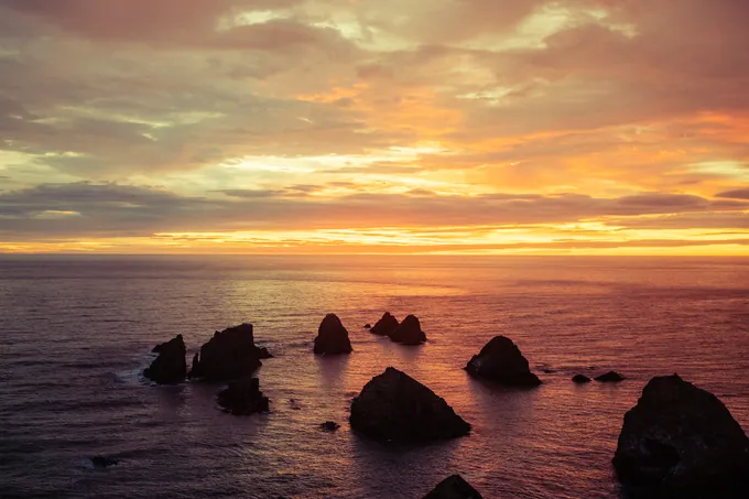 Farallones recortados en un mar en calma bajo un atardecer naranja y rosa
